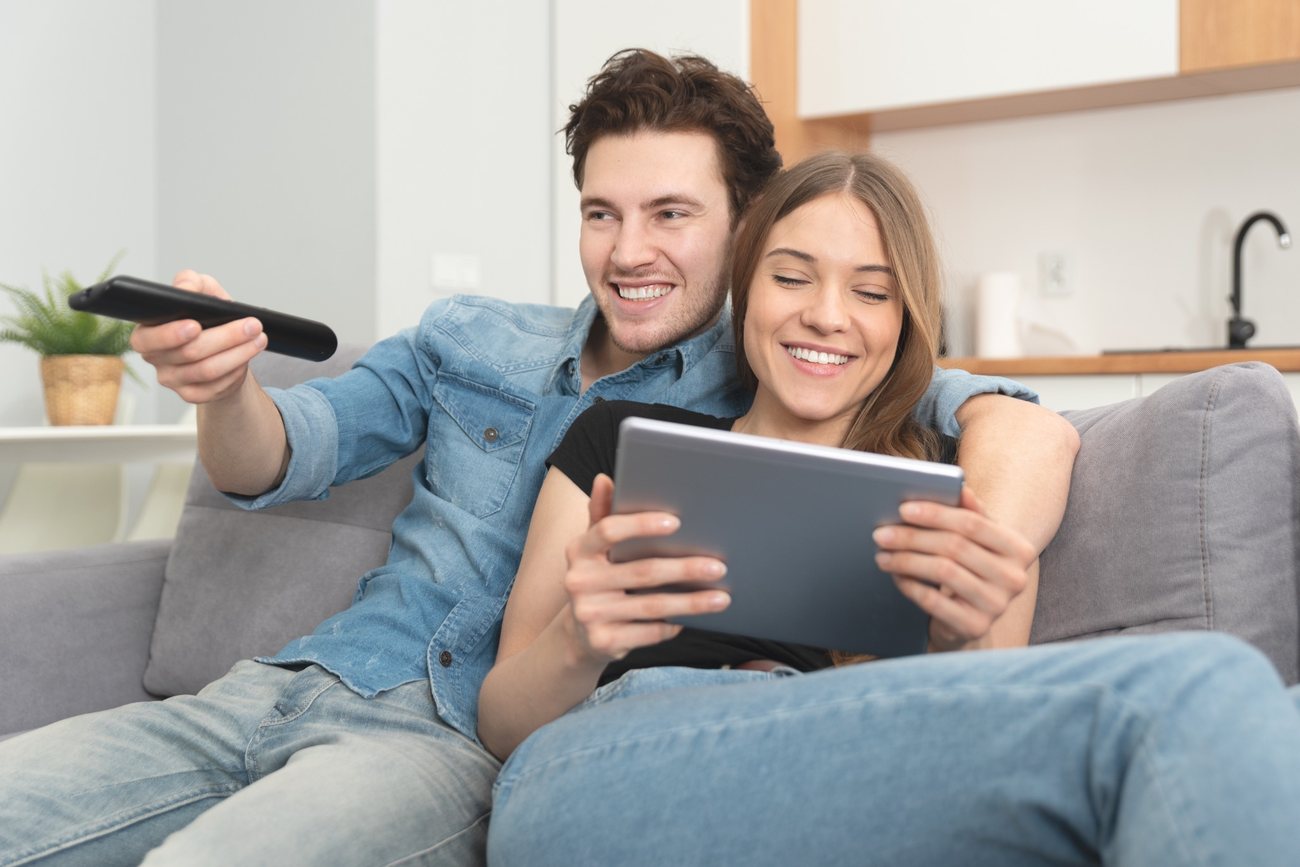 Cuplu urmărind televizorul și folosind o tabletă